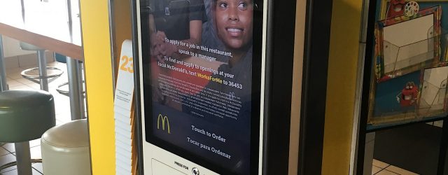 Picture of mcdonalds self ordering kiosk with digital ad displayed that says "now hiring"