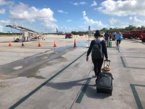 Walking across runway to the plane, boarding outdoors with carry on suitcase